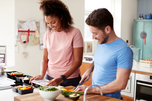 A man and woman are collaboratively preparing food in a modern kitchen, surrounded by fresh ingredients and cooking utensils. - Fitsse