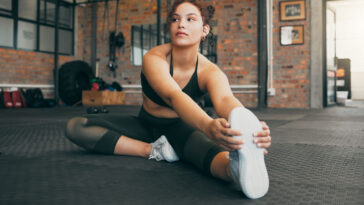 An adult female person doing Pilates exercises while sitting on a wheel, focusing on her face and shoes.