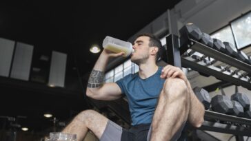 A person holding a bottle of alcohol and a shaker preparing a beverage for drinking.